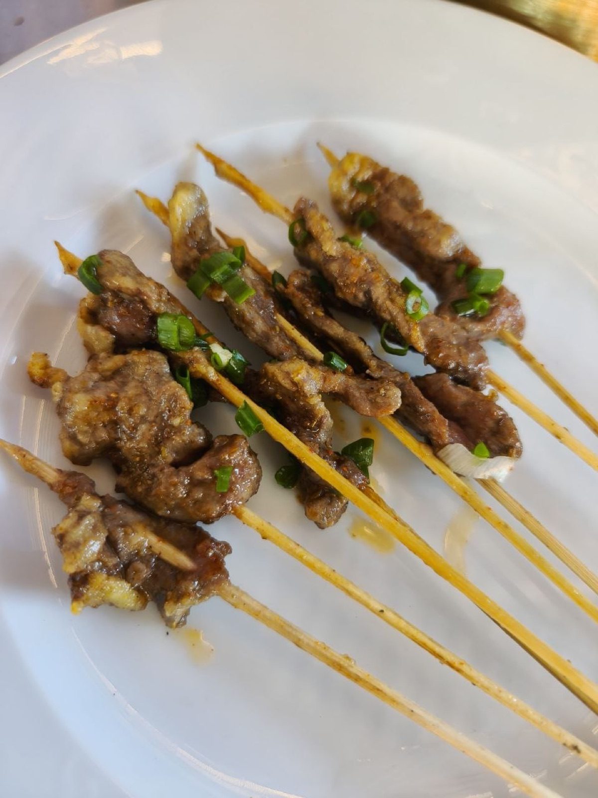 白瓷盤上撒上蔥花的烤牛肉串肉串